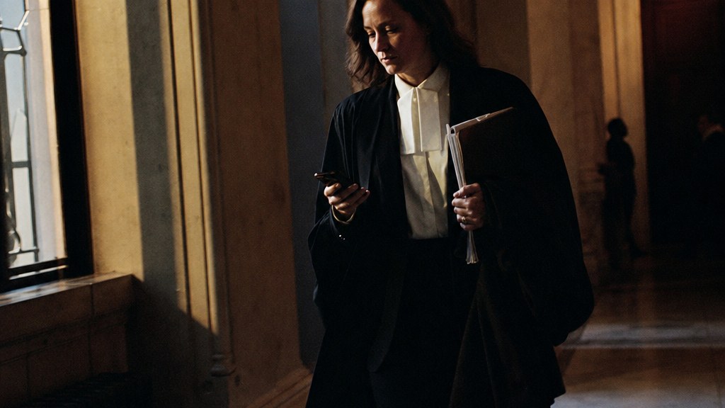 Family lawyer walking a courthouse corridor at dusk carrying a case file, phone in the other hand