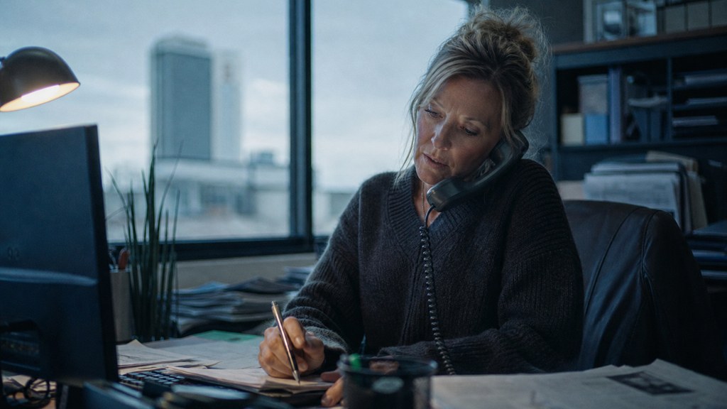An office manager at a cluttered desk with a landline handset tucked under one ear, photographed in Wichita