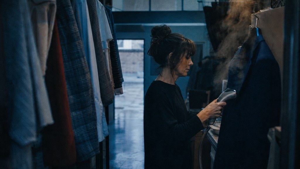 A boutique owner steaming garments in a narrow shop stockroom at opening time, photographed in Belfast
