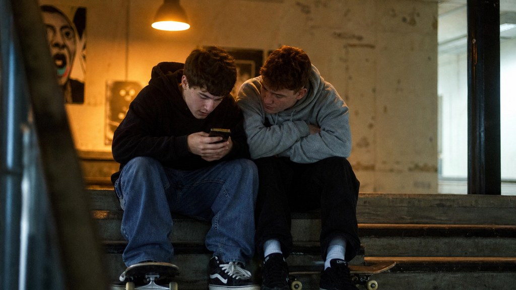 Two teenagers on skateboards looking at a phone on a set of concrete steps, photographed in Belfast