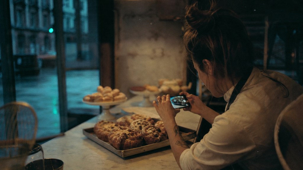 A bakery owner photographing a tray of pastries on a marble counter at dawn, photographed in Belfast