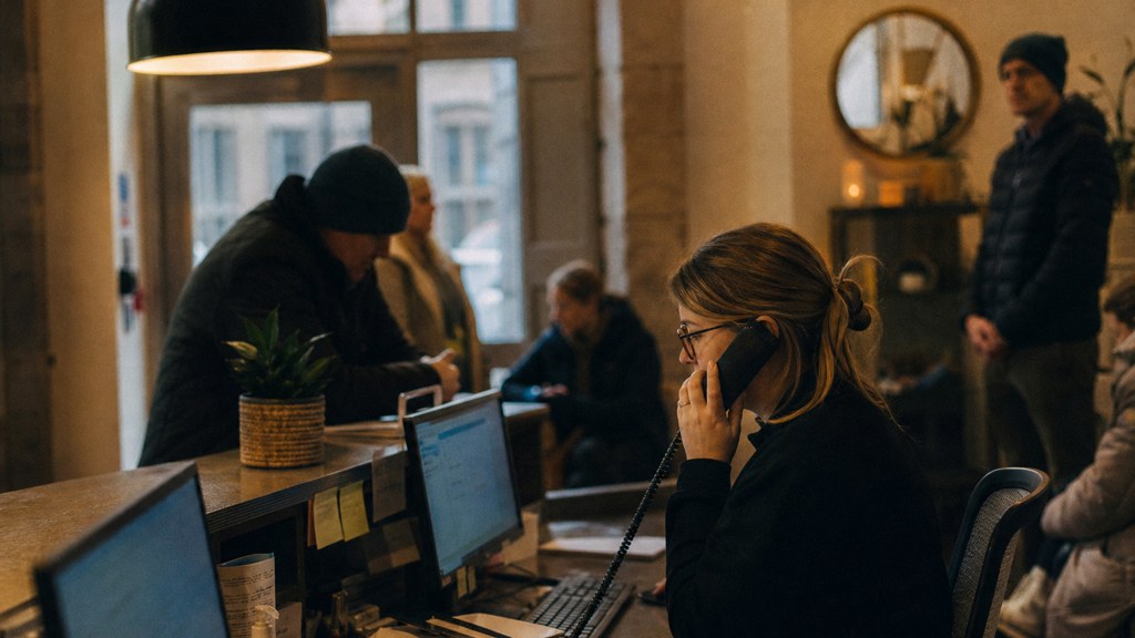 A clinic receptionist taking a phone call at a busy front desk with patients waiting, photographed in Bristol