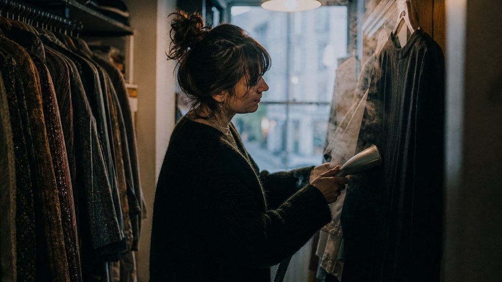 A boutique owner steaming garments in a narrow shop stockroom at opening time, photographed in Bristol