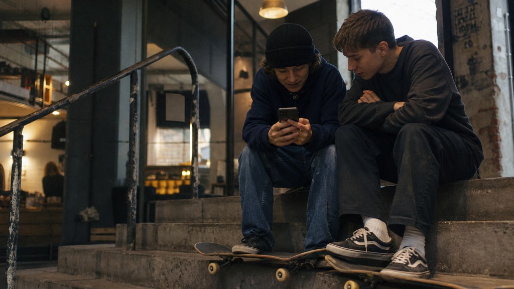 Two teenagers on skateboards looking at a phone on a set of concrete steps, photographed in Bristol