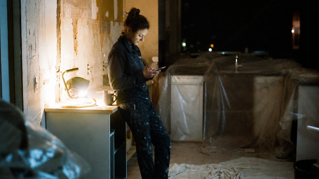 Boutique studio owner leaning on the reception counter reading a new trial booking notification on her phone