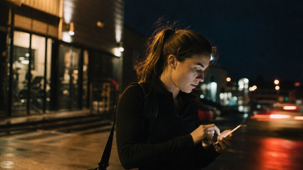 Woman in a gym car park at night tapping an ad on her phone for a free trial week