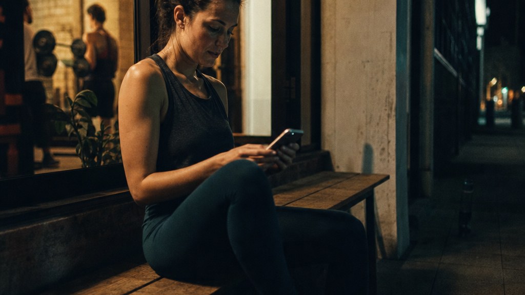 Prospective member sitting on a bench outside a fitness studio trying to load class times on her phone