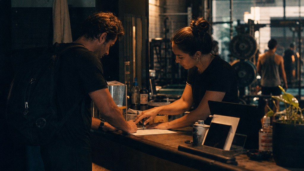 Gym front-desk worker helping a walk-in fill in a paper form after the website booking failed