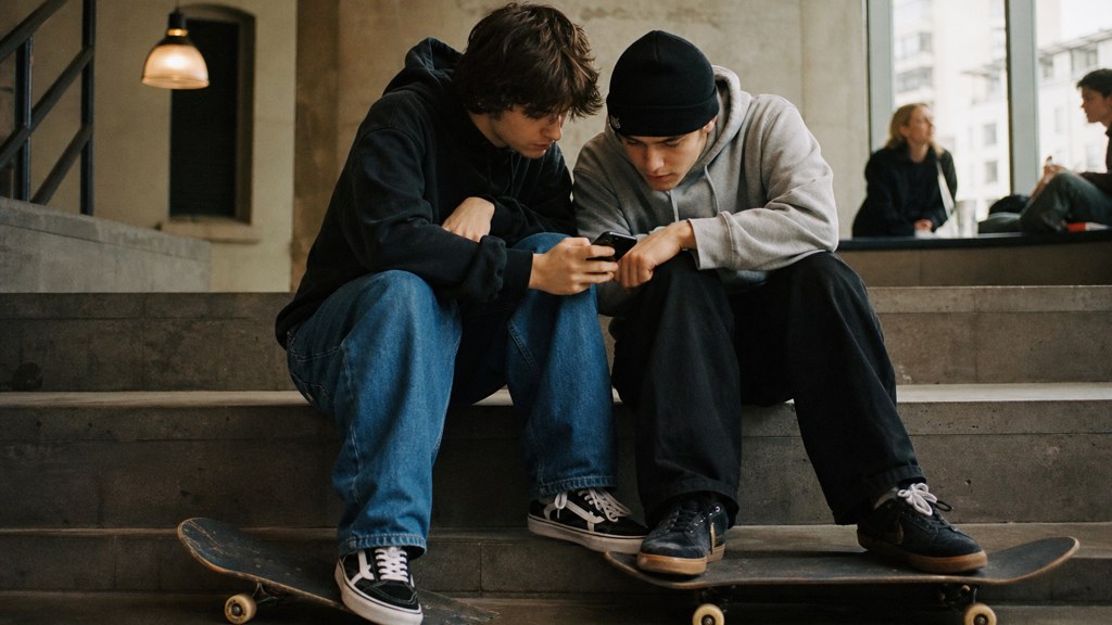 Two teenagers on skateboards looking at a phone on a set of concrete steps, photographed in Cardiff