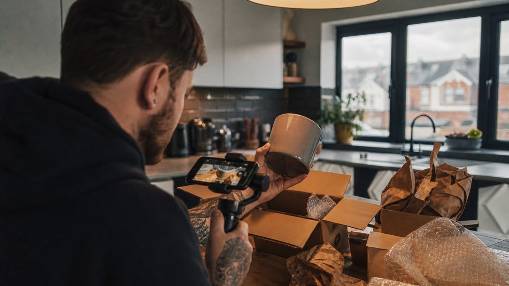 A customer filming an unboxing on a kitchen table strewn with packaging, photographed in Cardiff