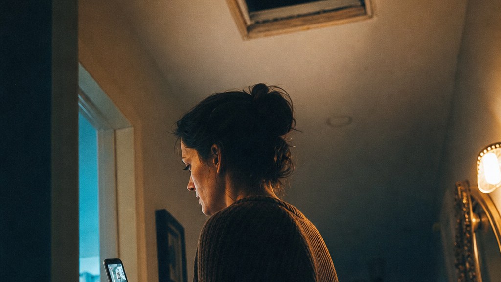 Homeowner watching a short technician video on her phone in a hallway beside an open vent