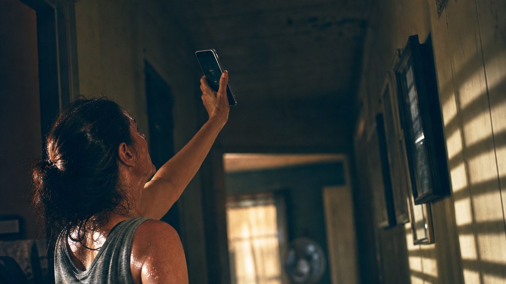 Homeowner in a sweltering hallway holding a phone up to a silent wall vent
