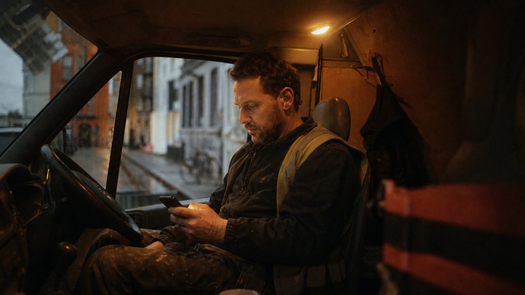 A contractor sitting in the cab of a work van reviewing a phone before driving off, photographed in Dublin