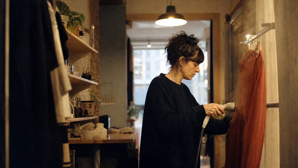 A boutique owner steaming garments in a narrow shop stockroom at opening time, photographed in Edinburgh
