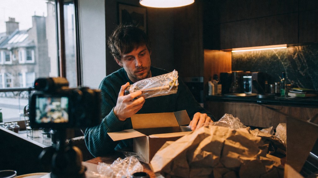 A customer filming an unboxing on a kitchen table strewn with packaging, photographed in Edinburgh