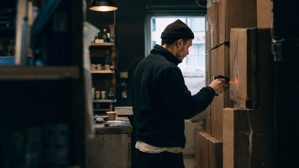 A seller checking barcodes on stacked cartons in a garage stockroom, photographed in Glasgow