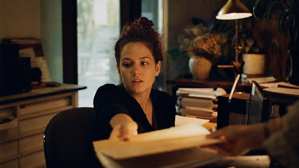 Practice receptionist handing a treatment folder across the front desk in morning light