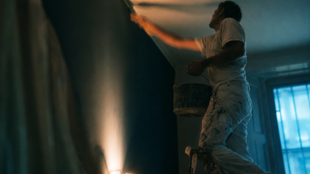 Painter cutting in a ceiling line from a stepladder, seen from below with his arm in motion