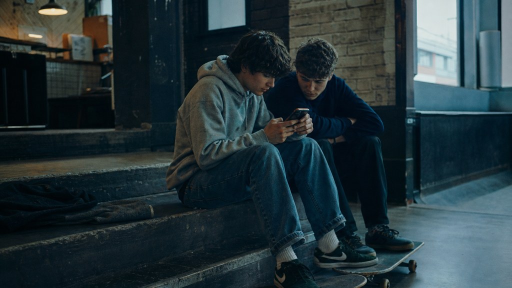 Two teenagers on skateboards looking at a phone on a set of concrete steps, photographed in Liverpool