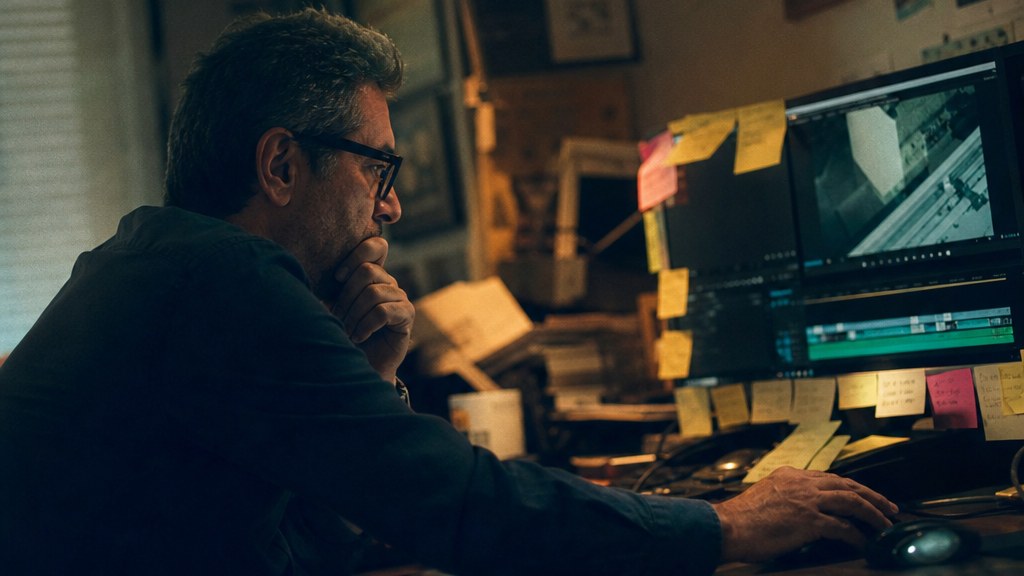 Editor in a cluttered edit suite scrubbing a timeline with sticky notes ringing the monitor bezel