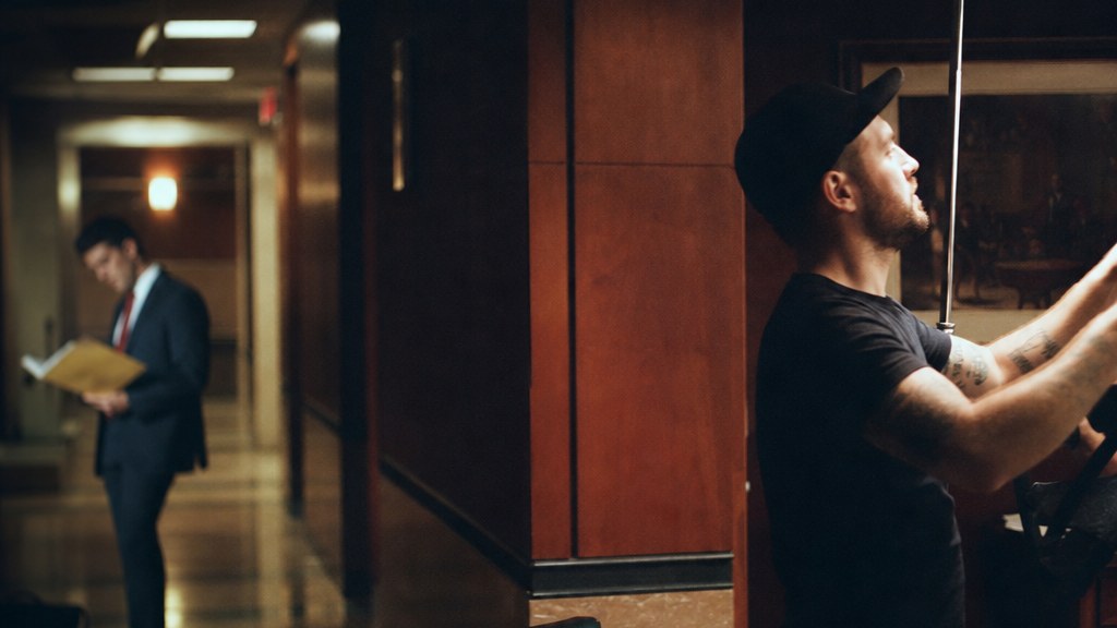 Film crew member adjusting a light stand in a real law office lobby with a lawyer waiting out of focus to one side