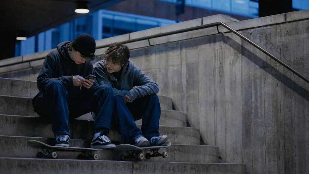Two teenagers on skateboards looking at a phone on a set of concrete steps, photographed in Manchester