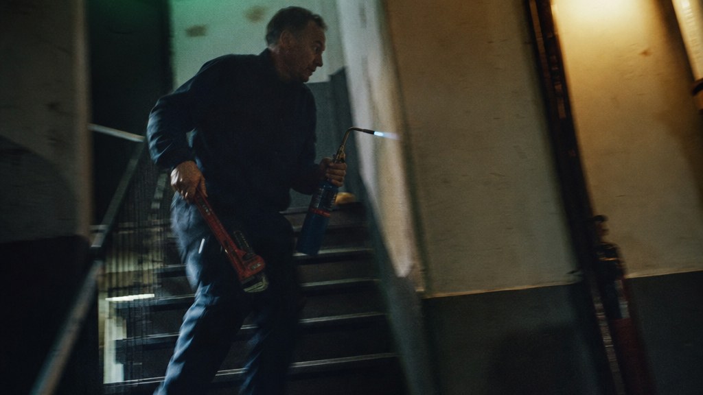 Plumber running down an apartment stairwell at night with a wrench and torch