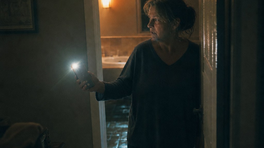 Homeowner in a dark bathroom doorway holding a phone with the torch on