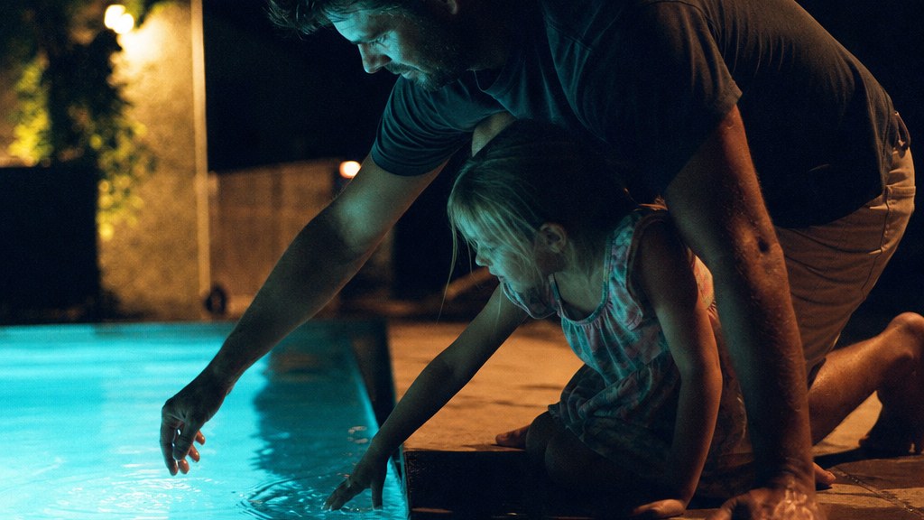 Father and daughter kneeling at the edge of a freshly filled pool lit turquoise at night