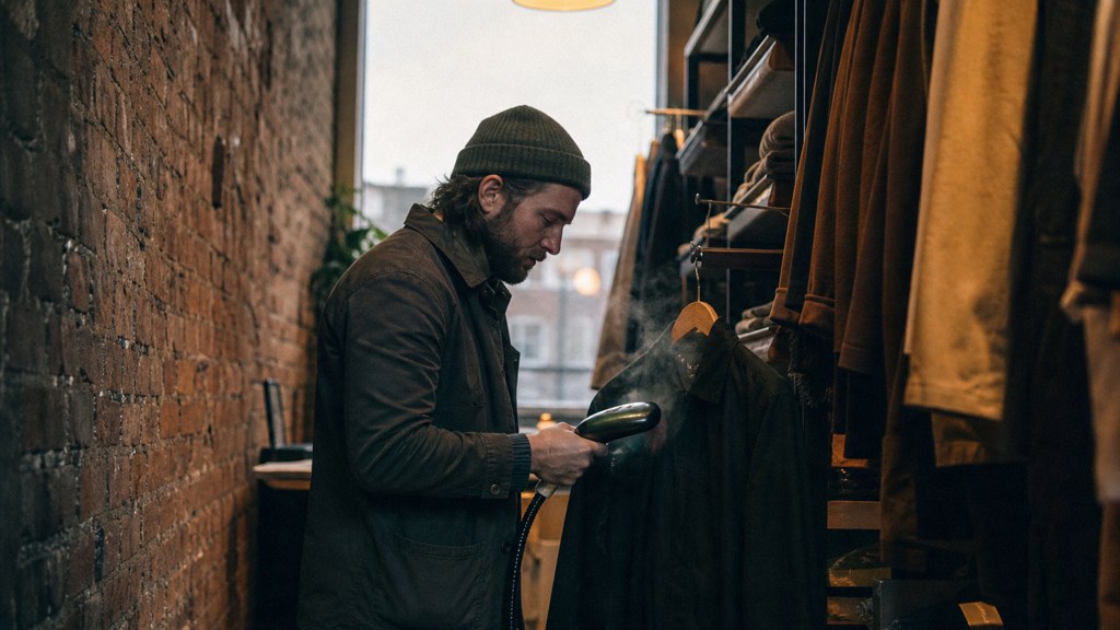 A boutique owner steaming garments in a narrow shop stockroom at opening time, photographed in Sheffield