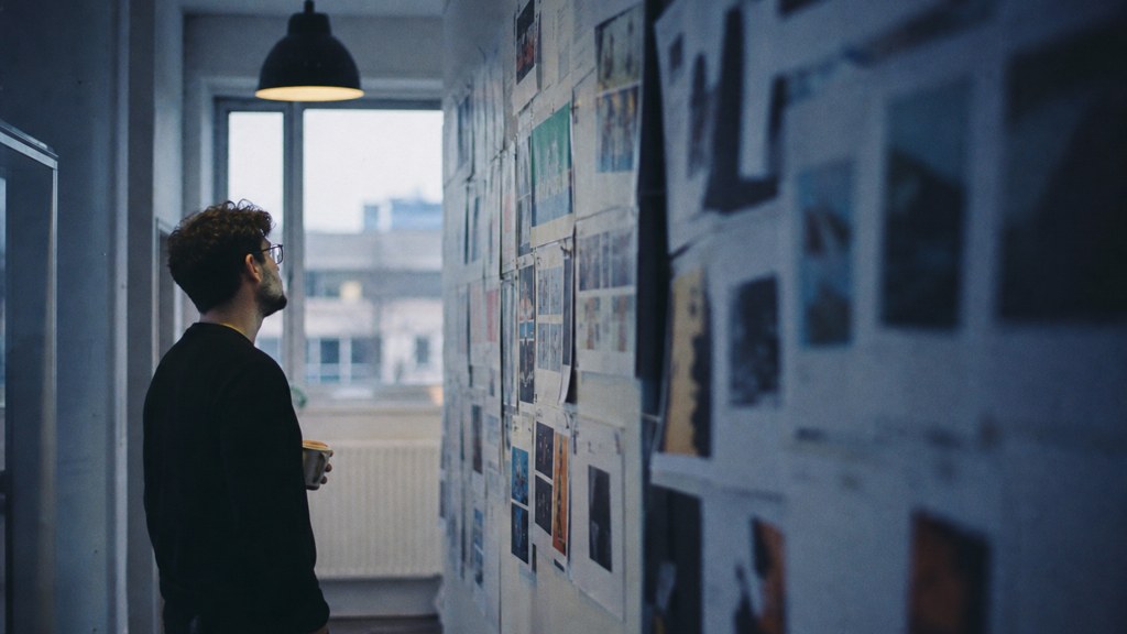 A media planner standing at a wall of printed layouts in a narrow agency corridor, photographed in Sheffield
