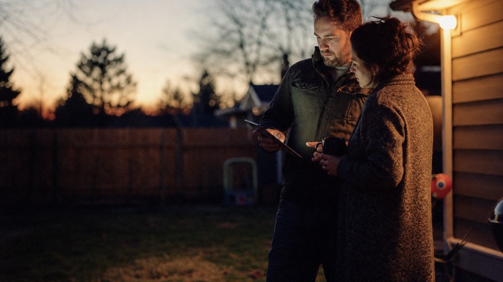 Couple standing at the edge of an empty backyard at sunset holding a tablet