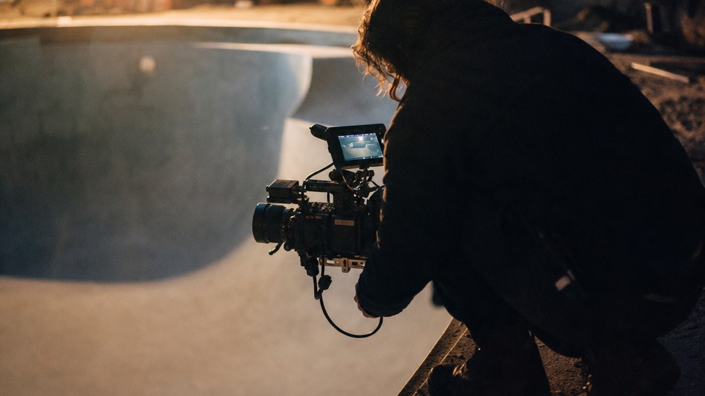 Camera operator crouching at the lip of a freshly gunited pool shell in low sun