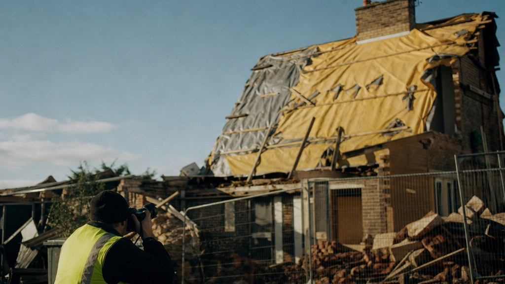 Photographer kneeling on a driveway shooting a half-stripped roof