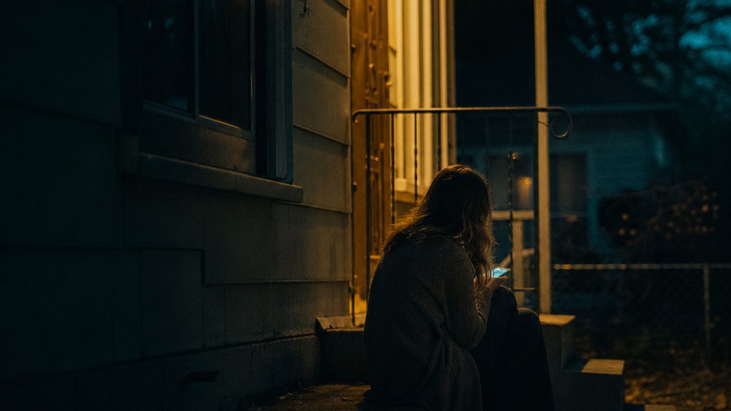 Woman on a porch step at night lit by her phone screen