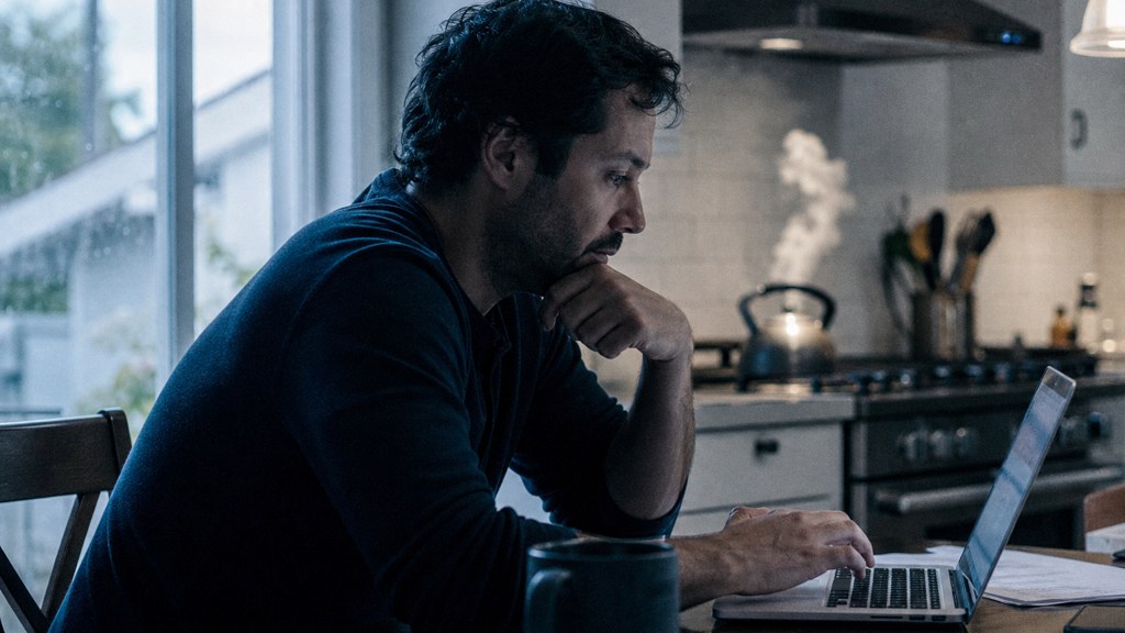 A service-business owner at a kitchen table typing a question into a laptop while a kettle steams behind, photographed in Irvine