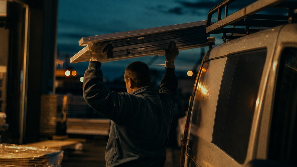 Warehouse hand loading panels onto a van rack before dawn