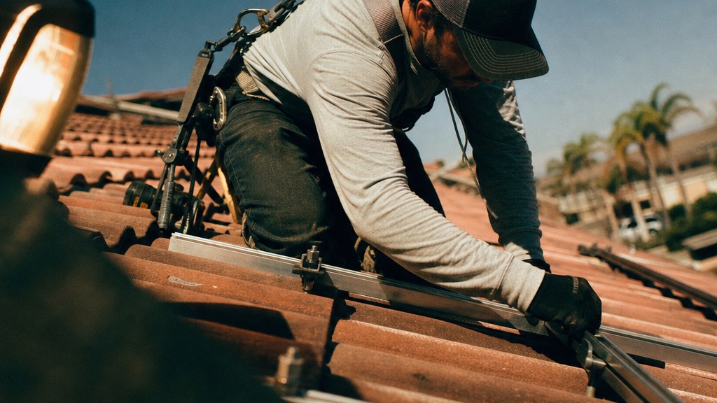 Solar installer kneeling on a hot tile roof checking a rail alignment at midday