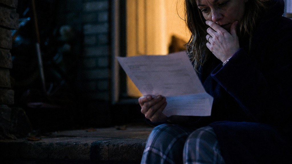Homeowner holding a paper utility bill on a doorstep in late light