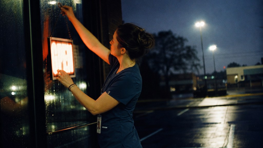 Nurse practitioner switching on an urgent care open sign before dawn in the rain