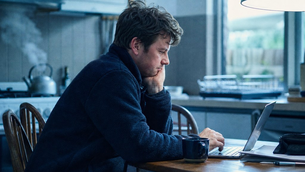 A service-business owner at a kitchen table typing a question into a laptop while a kettle steams behind, photographed in Melbourne