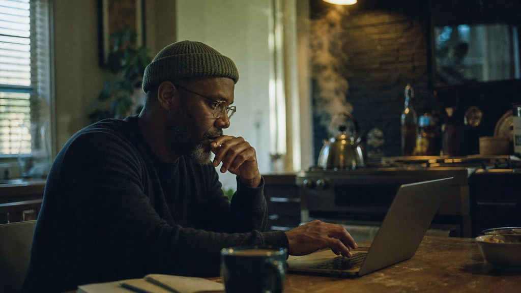 A service-business owner at a kitchen table typing a question into a laptop while a kettle steams behind, photographed in Memphis