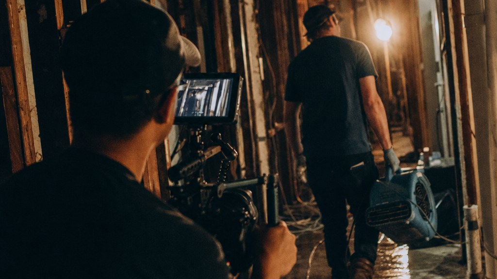Videographer filming a restoration technician carrying an air mover through a gutted hallway