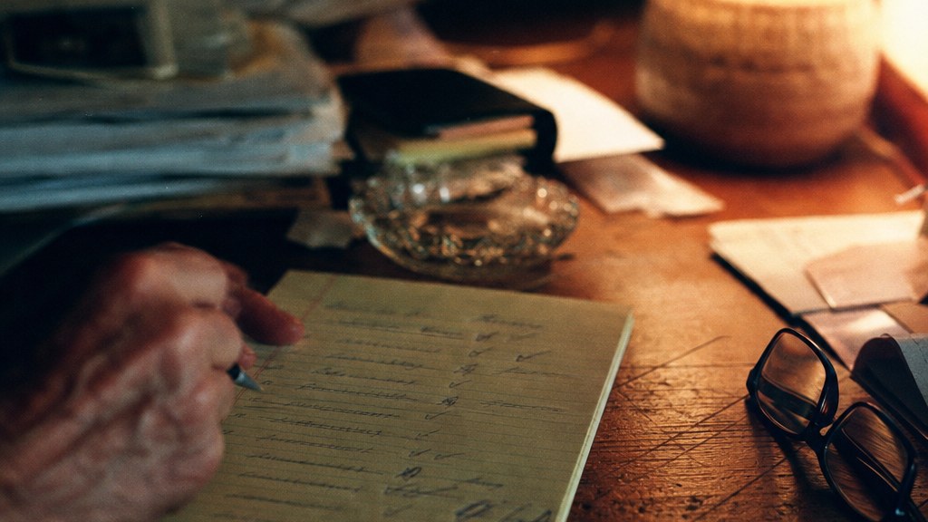 Close crop of a hand-annotated estate planning checklist beside folded reading glasses on a walnut table