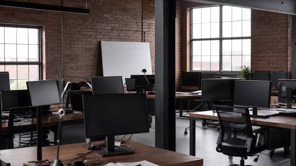 Editorial photograph of an empty modern marketing analytics studio in a Hamilton Ontario brick industrial conversion with heavy timber beams and cool flat northern light, a widescreen monitor showing a blank dashboard and a tag manager container, a keyboard and a mug on a wooden desk, no people and no signage