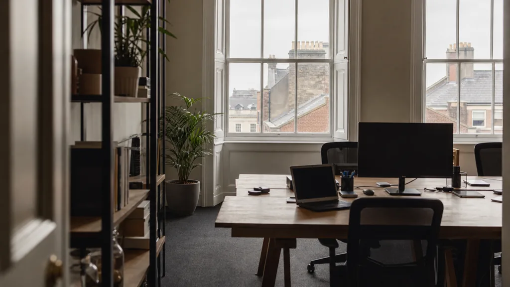 Editorial photograph of an empty marketing agency workspace in a Dublin Georgian building with sash windows onto brick rooftops and soft grey daylight