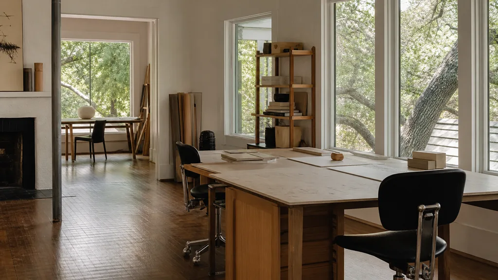 Editorial photograph of an empty design studio workspace in an Austin converted bungalow with wooden floors and windows onto live oaks