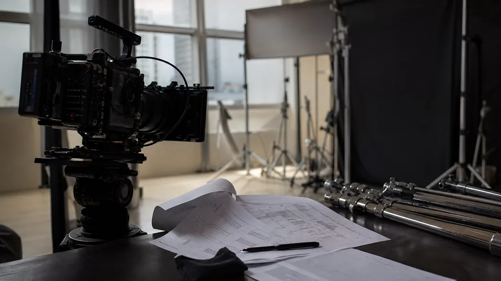 Editorial photograph of a Hong Kong video production studio with a cinema camera, printed call sheets and lighting stands on a dark table