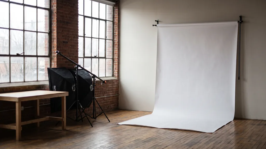 Editorial photograph of an empty photography studio corner with a white seamless paper sweep, a bare shooting table and switched-off softbox lighting