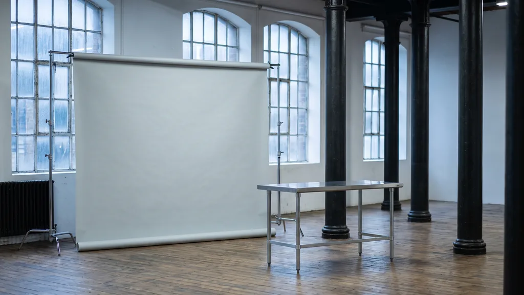 Editorial photograph of an empty photography studio in a Liverpool dock warehouse with cast-iron columns, a pale grey paper sweep and a plain steel shooting table, no people and no signage